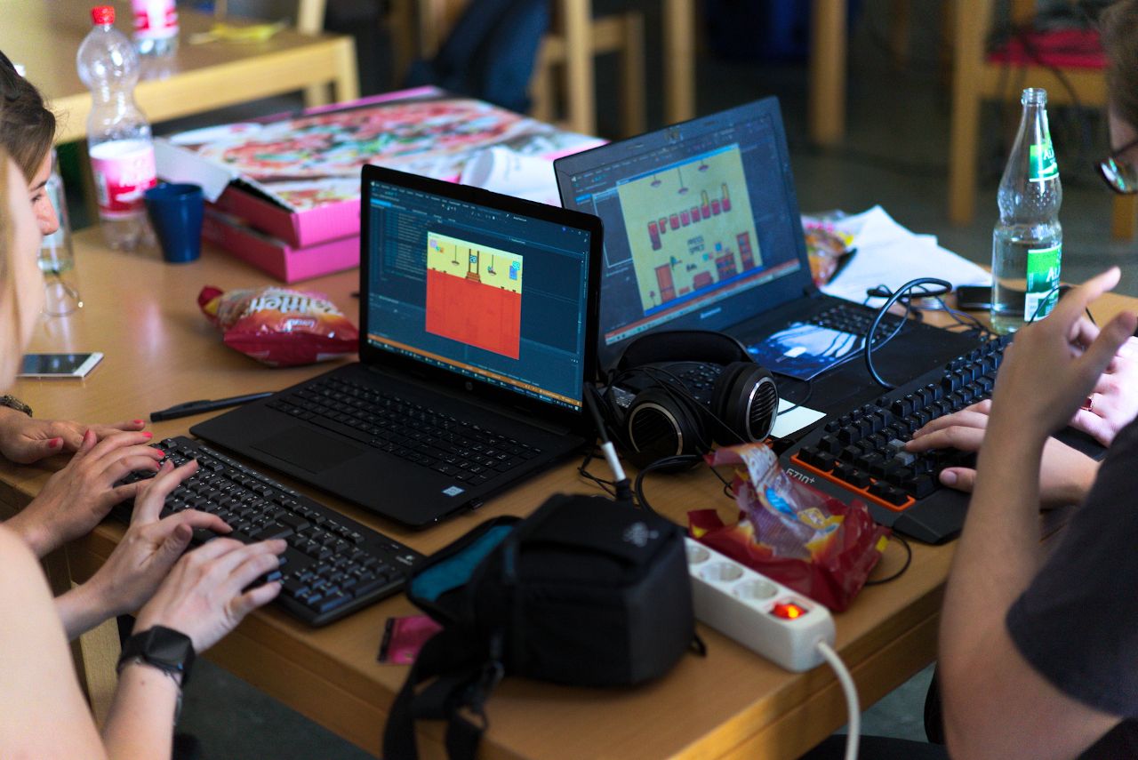 Zu sehen sind 2 Laptops auf einem Tisch, die von drei Personen bedient werden.