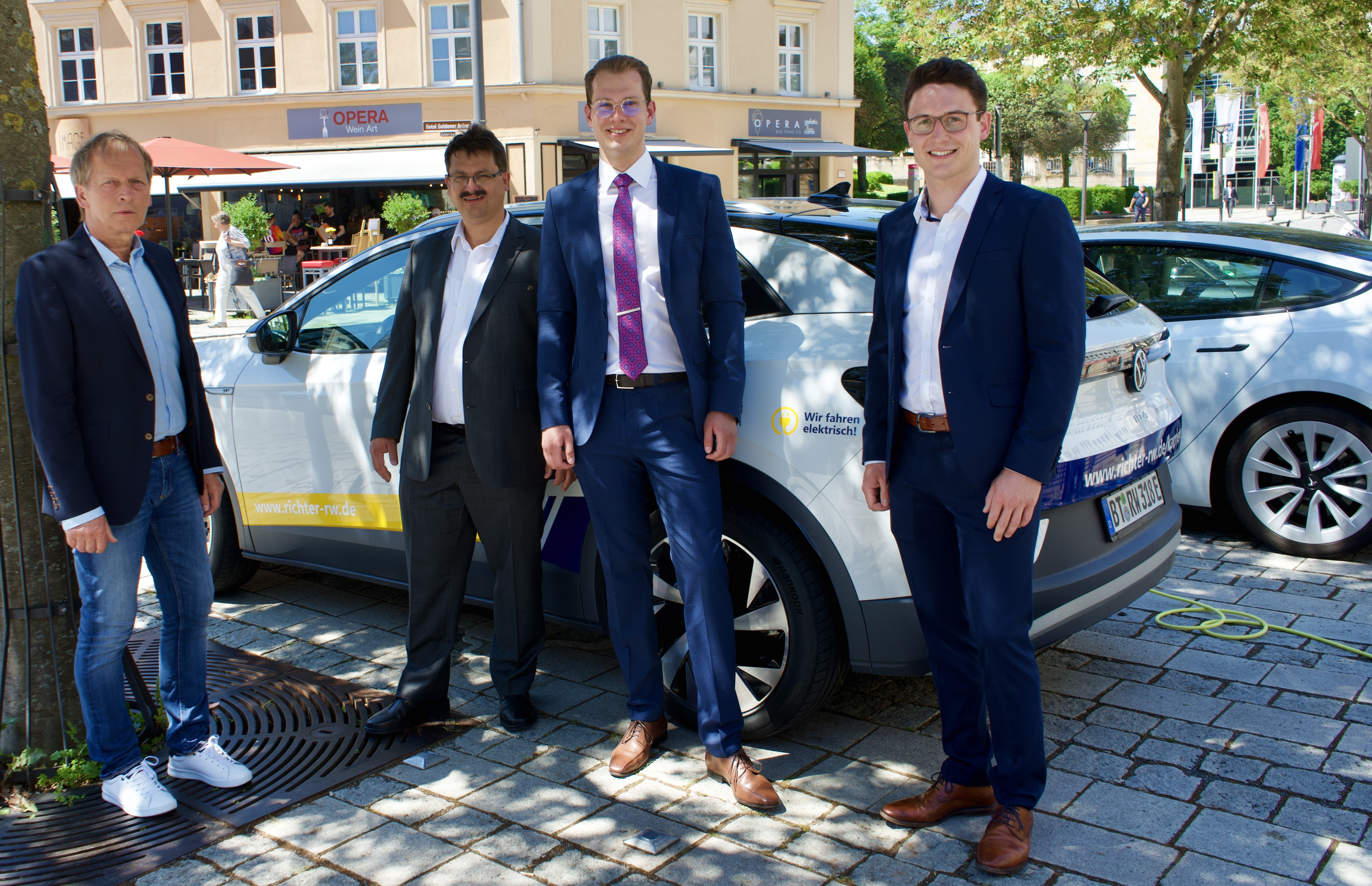 Vier Männer im Anzug stehen vor einem Elektroauto in Bayreuth